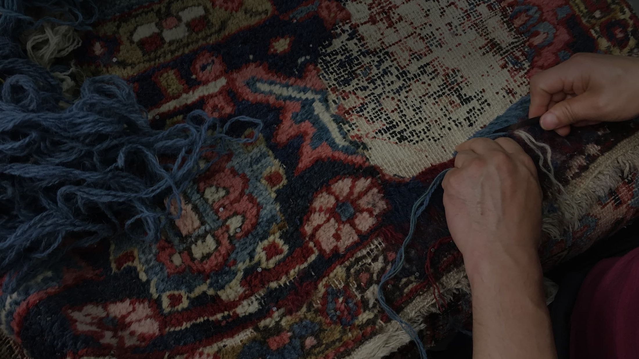 Ein Teppich wird repariert - ein Paar Hände nähen eine ausgefranste Stelle am Orientteppich.